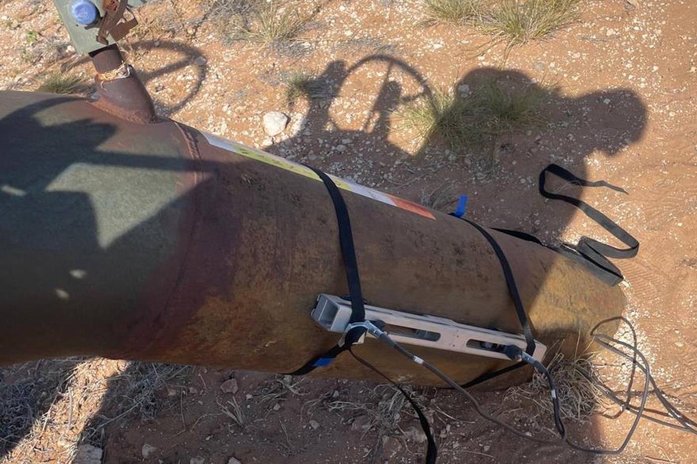 Portable clamp-on flow meter strapped to a remote pipeline riser with a manual valve and no mains power